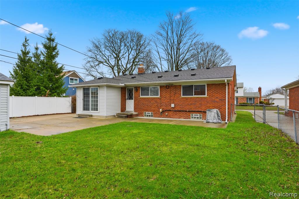 Rear view of house with a fenced backyard, a patio area, brick siding, and a chimney