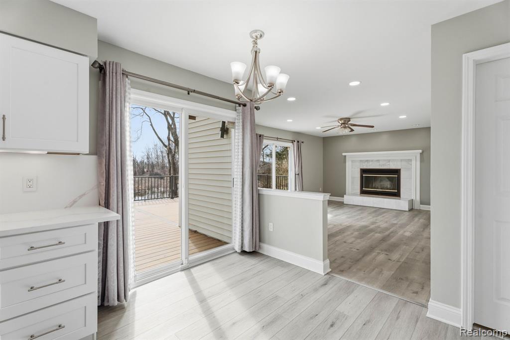 Unfurnished dining area with light wood-type flooring, a tiled fireplace, a chandelier, and ceiling fan