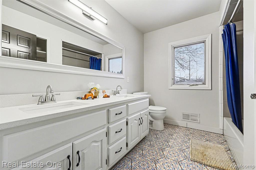 Full bathroom featuring double vanity, shower / bath combination with curtain, and light tile patterned flooring