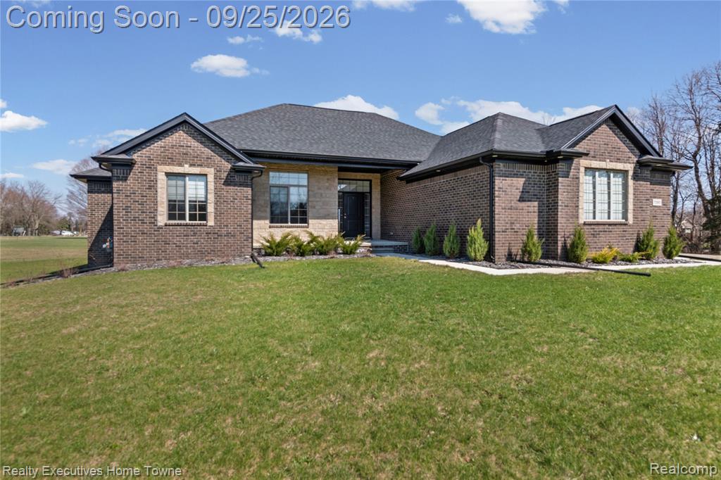 View of front of house with brick siding, a front lawn, and a shingled roof