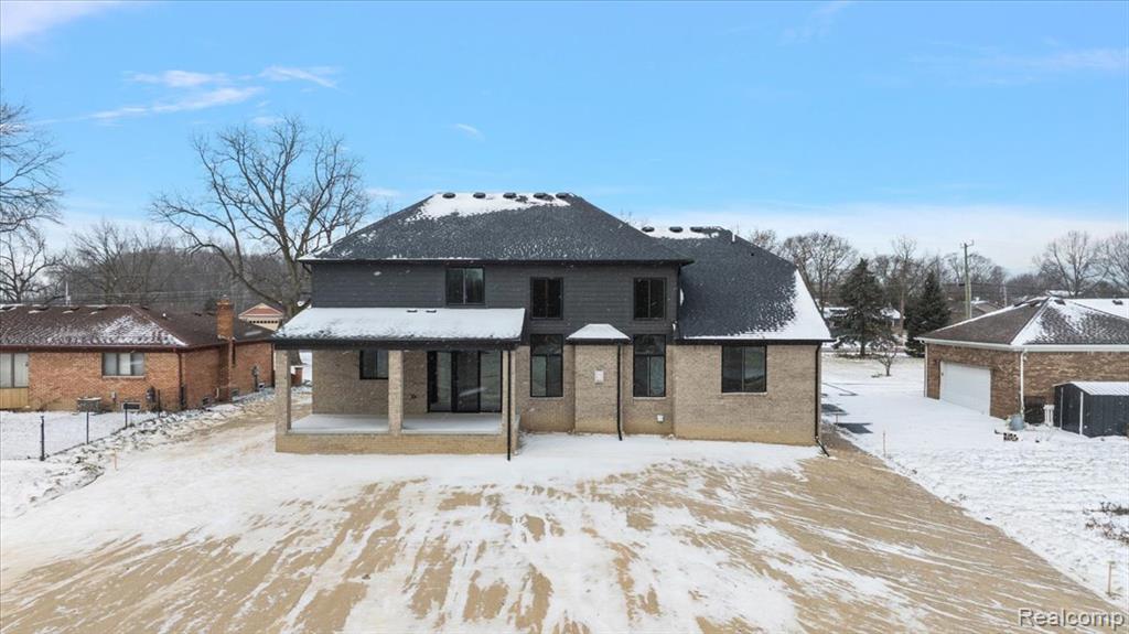 Snow covered back of property with a patio area and brick siding