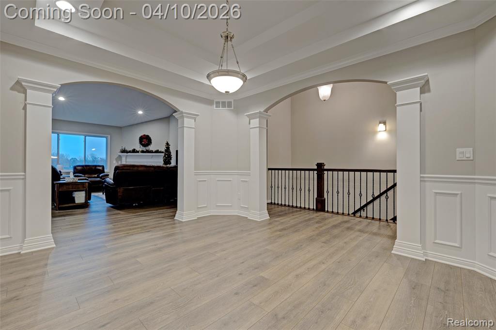 Empty room featuring arched walkways, wainscoting, a decorative wall, recessed lighting, and ornate columns