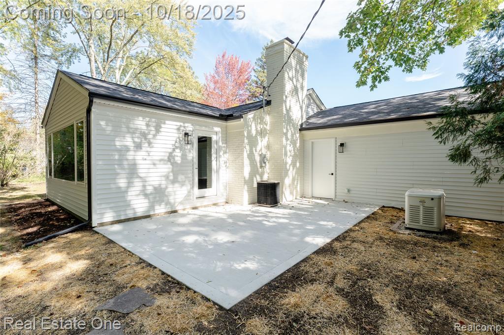 Back of property featuring a patio area, a chimney, and a shingled roof