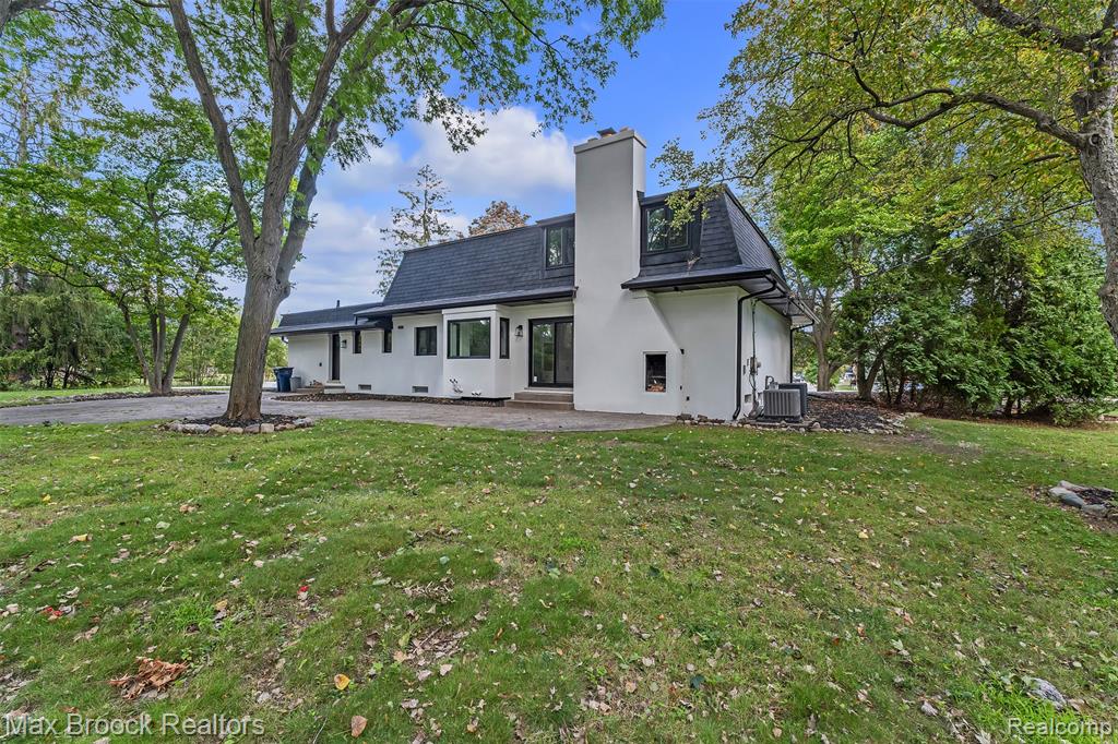 Back of house with a patio area, a yard, stucco siding, and mansard roof