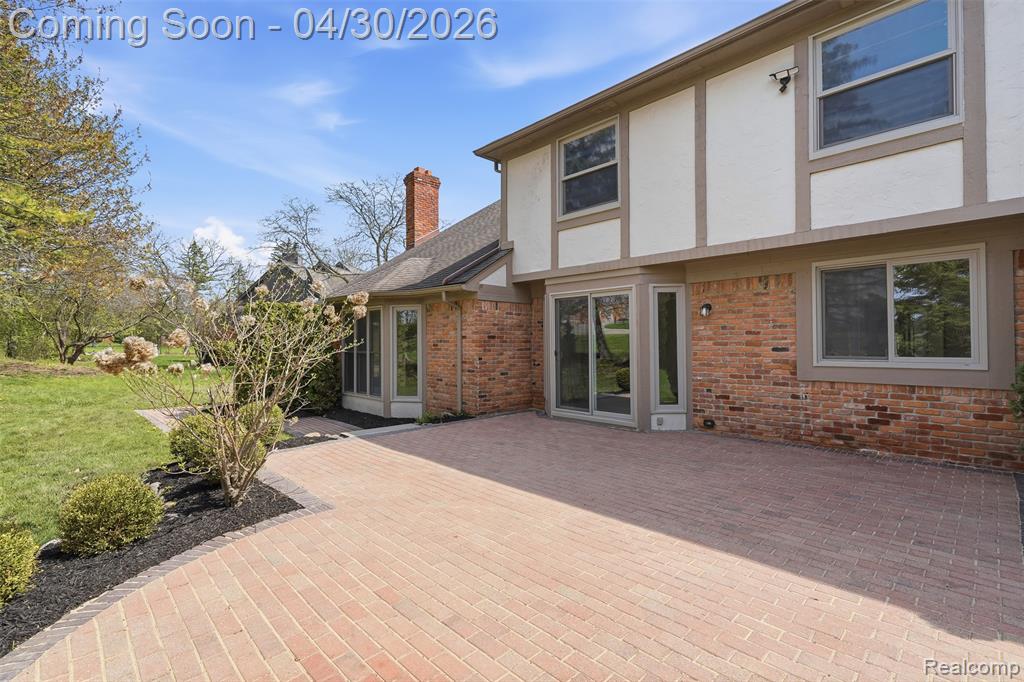 Rear view of house featuring stucco siding, brick siding, a patio area, a chimney, and a lawn