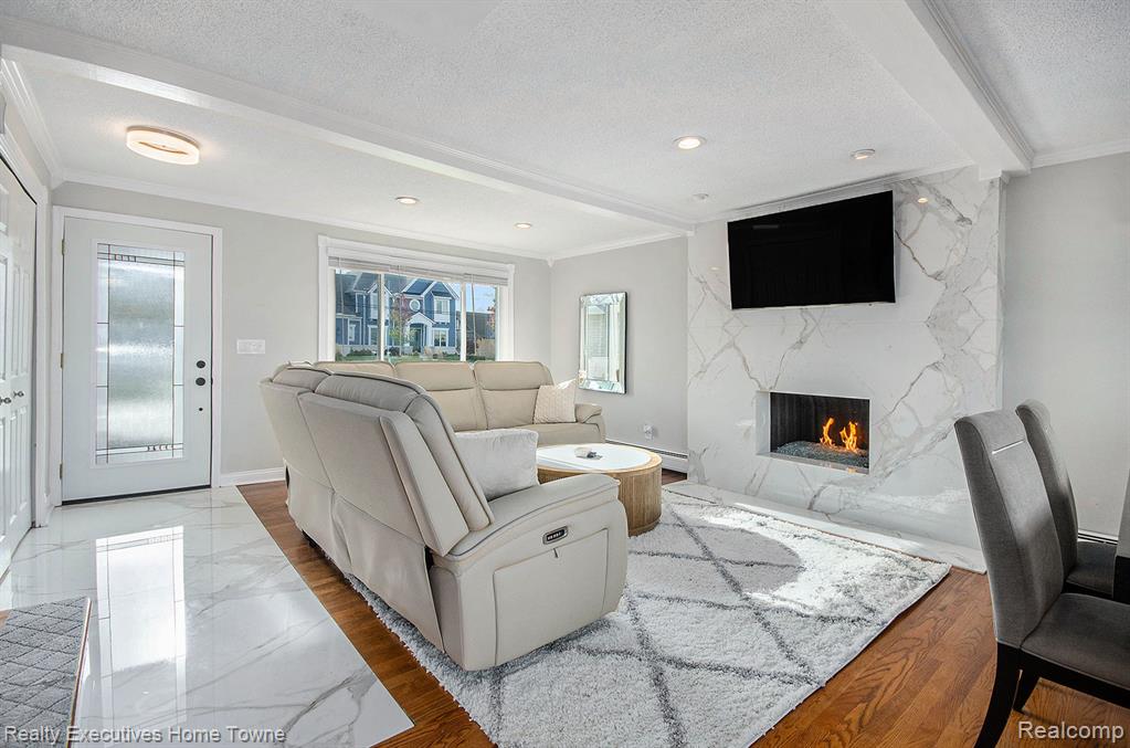 Living area featuring ornamental molding, a textured ceiling, a fireplace, wood finished floors, and beamed ceiling
