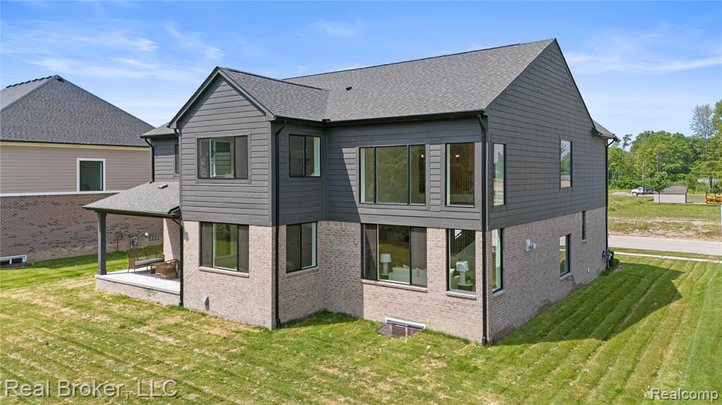 Back of house featuring brick siding, a yard, roof with shingles, and a patio area