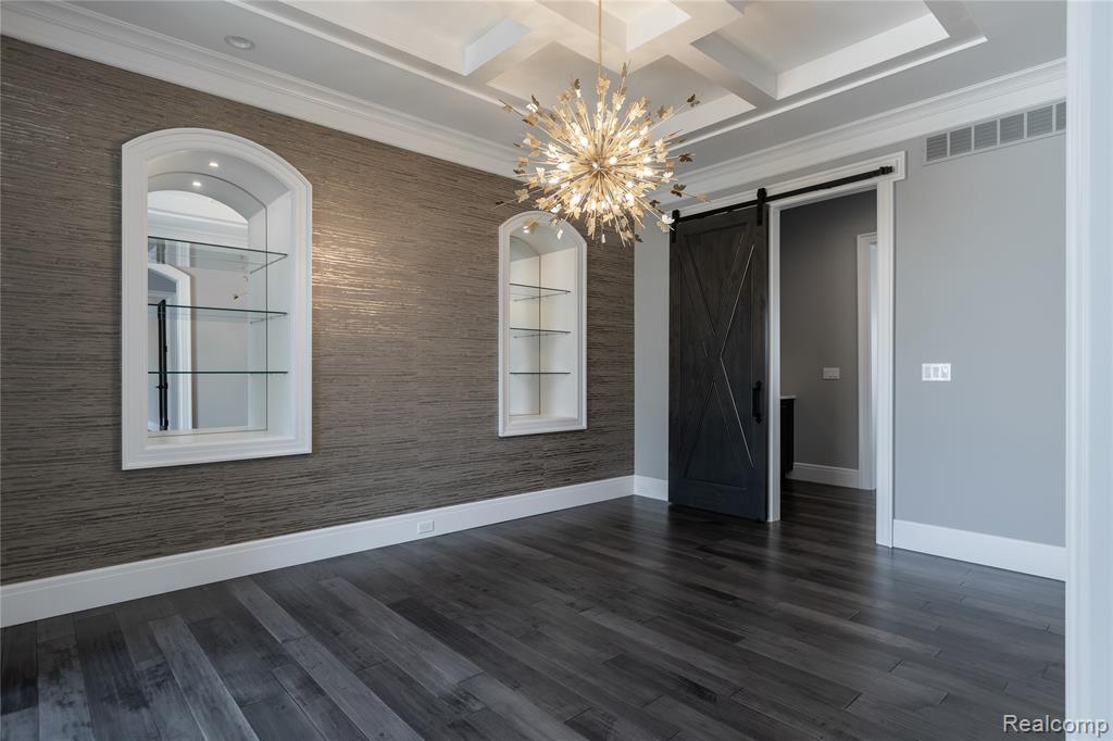 Spare room featuring a barn door, a chandelier, ornamental molding, coffered ceiling, and dark wood-style flooring