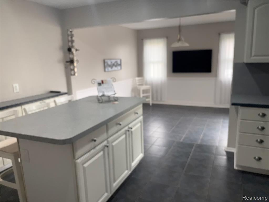 Kitchen featuring white cabinetry, a kitchen island, a breakfast bar, hanging light fixtures, and dark countertops