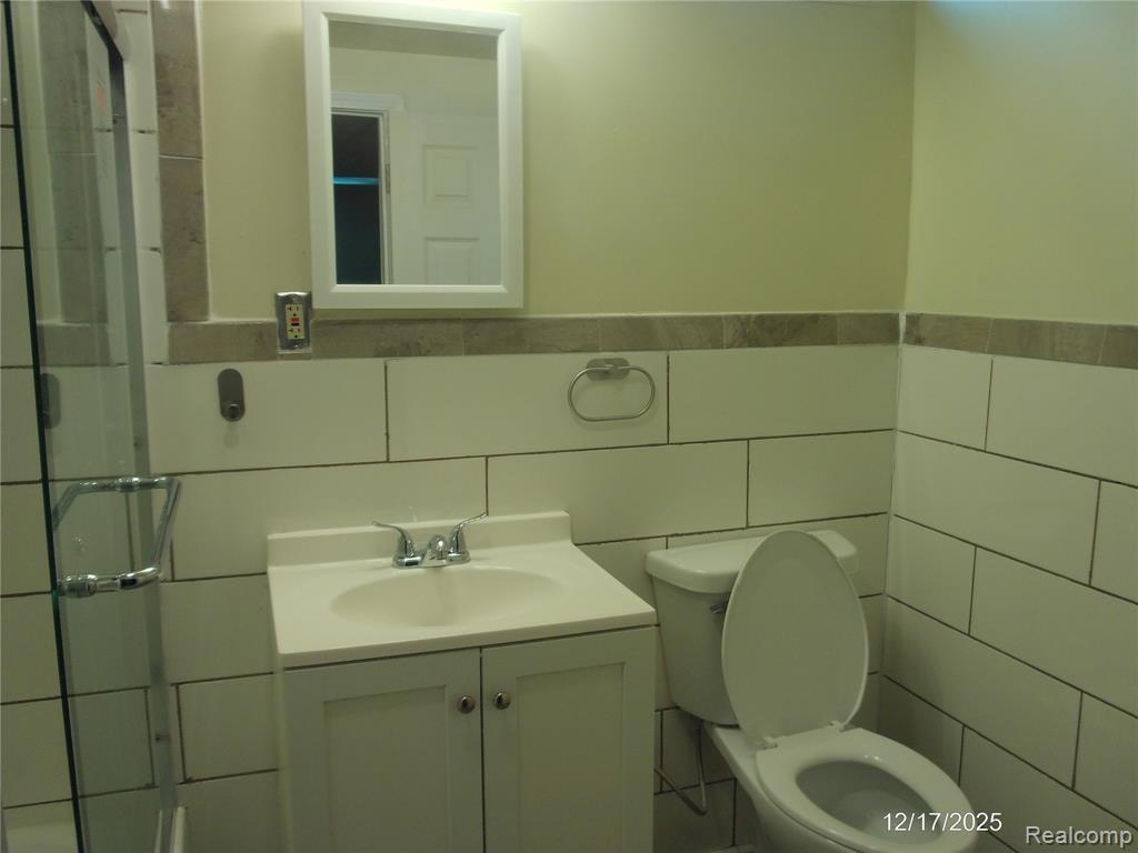 Full bath with tile walls, vanity, wainscoting, and a shower
