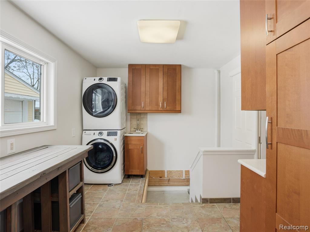 Laundry room with stacked washer and dryer, cabinet space, and light stone finish floors