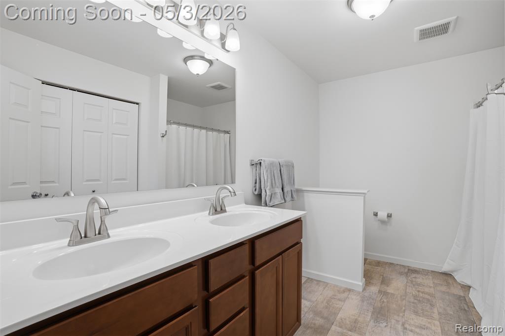 Full bathroom featuring double vanity, light wood-style flooring, a closet, and curtained shower