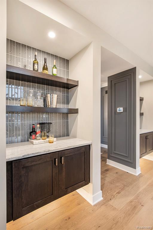 Bar area with open shelves, dark brown cabinets, light wood-type flooring, recessed lighting, and light stone counters