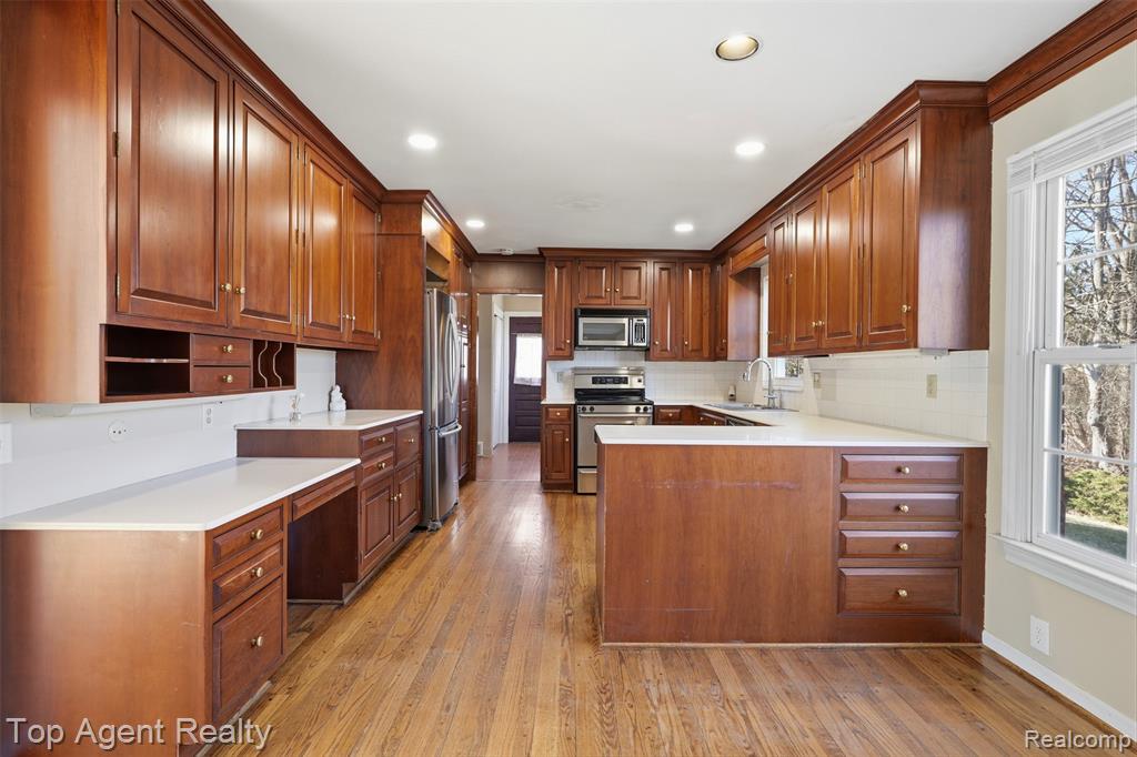 Kitchen featuring stainless steel appliances, tasteful backsplash, light countertops, wood finish cabinetry, and light wood-style floors