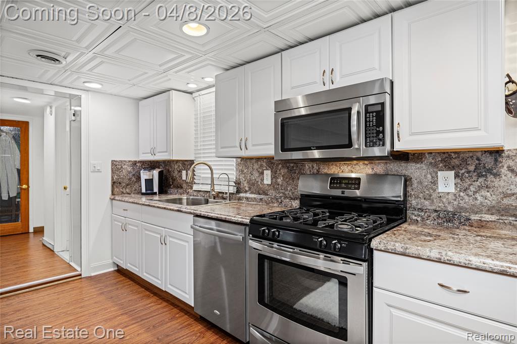 Kitchen featuring stainless steel appliances, white cabinets, light wood finished floors, light stone counters, and an ornate ceiling
