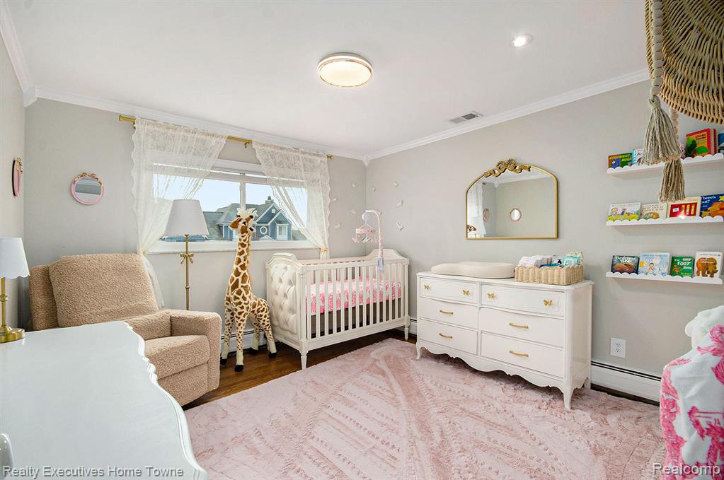 Bedroom with ornamental molding, a nursery area, a baseboard heating unit, and wood finished floors