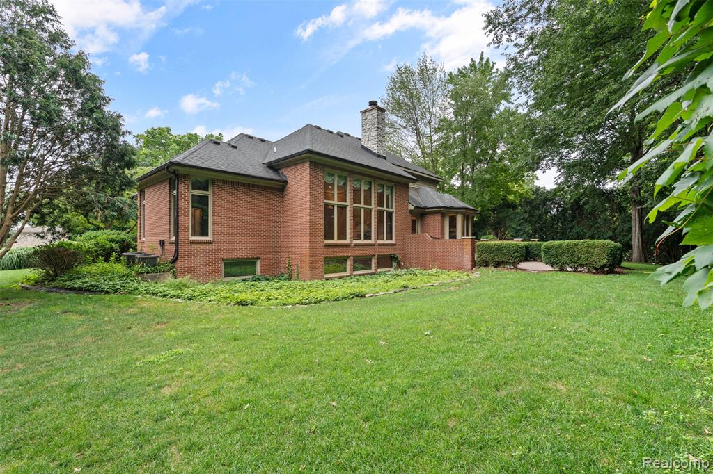 Rear view of house featuring brick siding, a chimney, and a yard