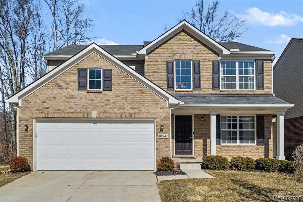 View of front of home with a porch, concrete driveway, brick siding, and a front yard