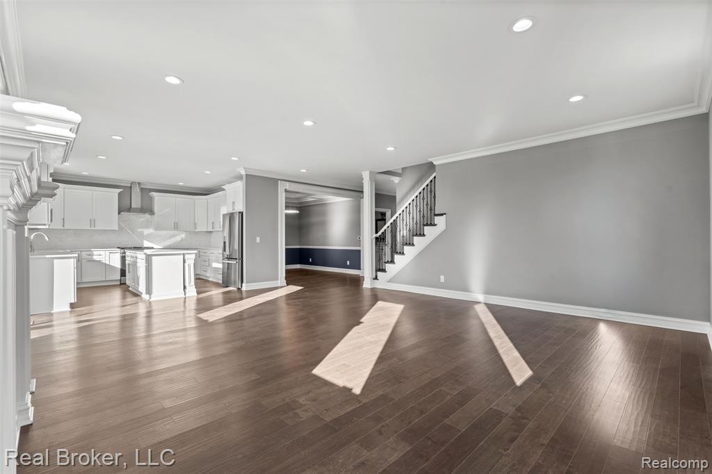 Unfurnished living room with stairs, dark wood finished floors, crown molding, and recessed lighting