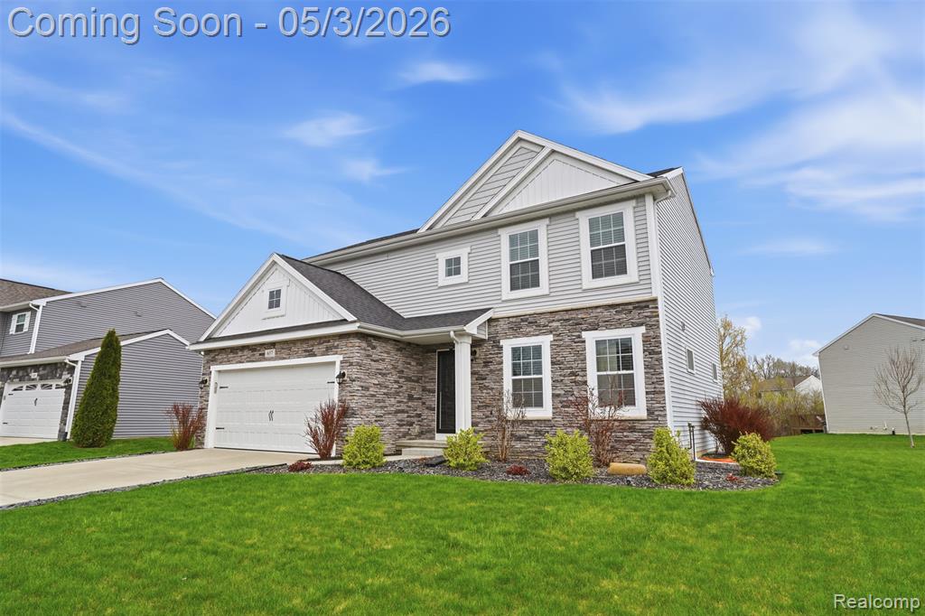 View of front of house featuring stone siding, a front lawn, driveway, and an attached garage