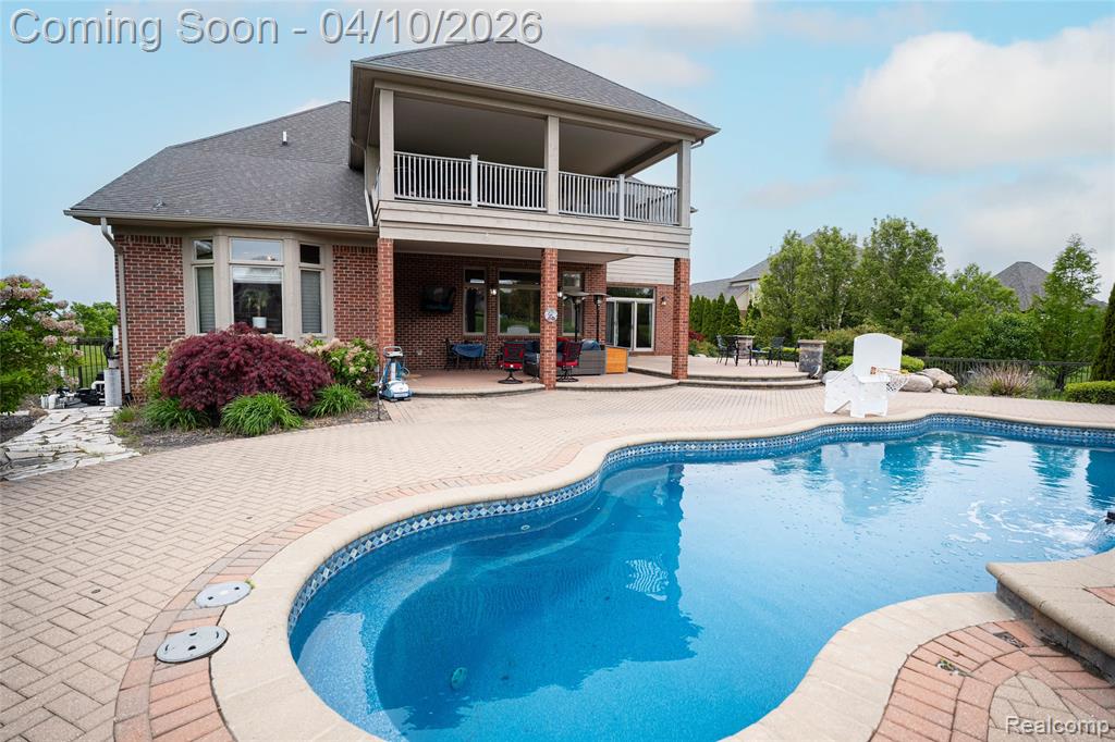 Rear view of house with a patio area, brick siding, a shingled roof, and a balcony