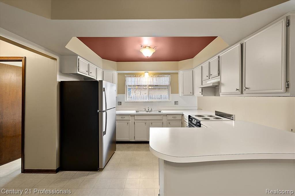 Kitchen with freestanding refrigerator, a peninsula, light countertops, white range with electric stovetop, and light flooring