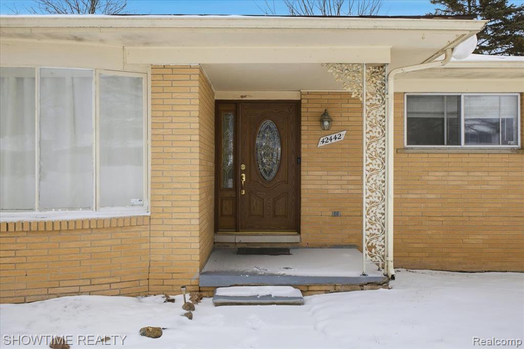 Snow covered property entrance with brick siding
