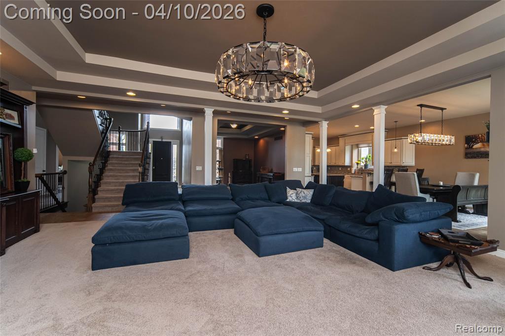 Living area with hanging lights, ornate columns, carpet floors, and a raised ceiling