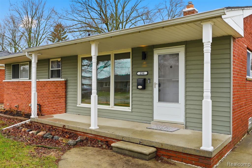 Doorway to property featuring covered porch, brick siding, and a chimney