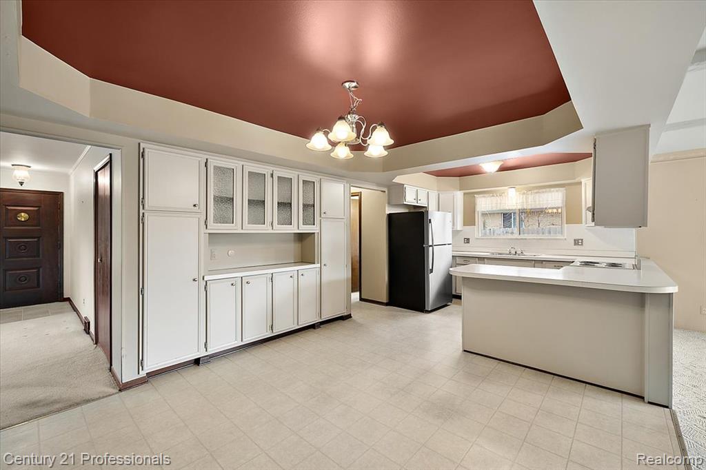 Kitchen with freestanding refrigerator, light countertops, white cabinetry, glass insert cabinets, and a chandelier