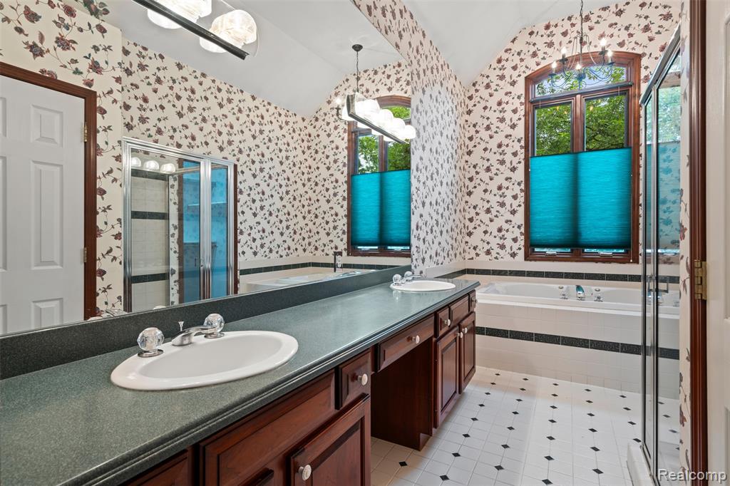 Full bath featuring wallpapered walls, double vanity, a bath, lofted ceiling, and a shower stall