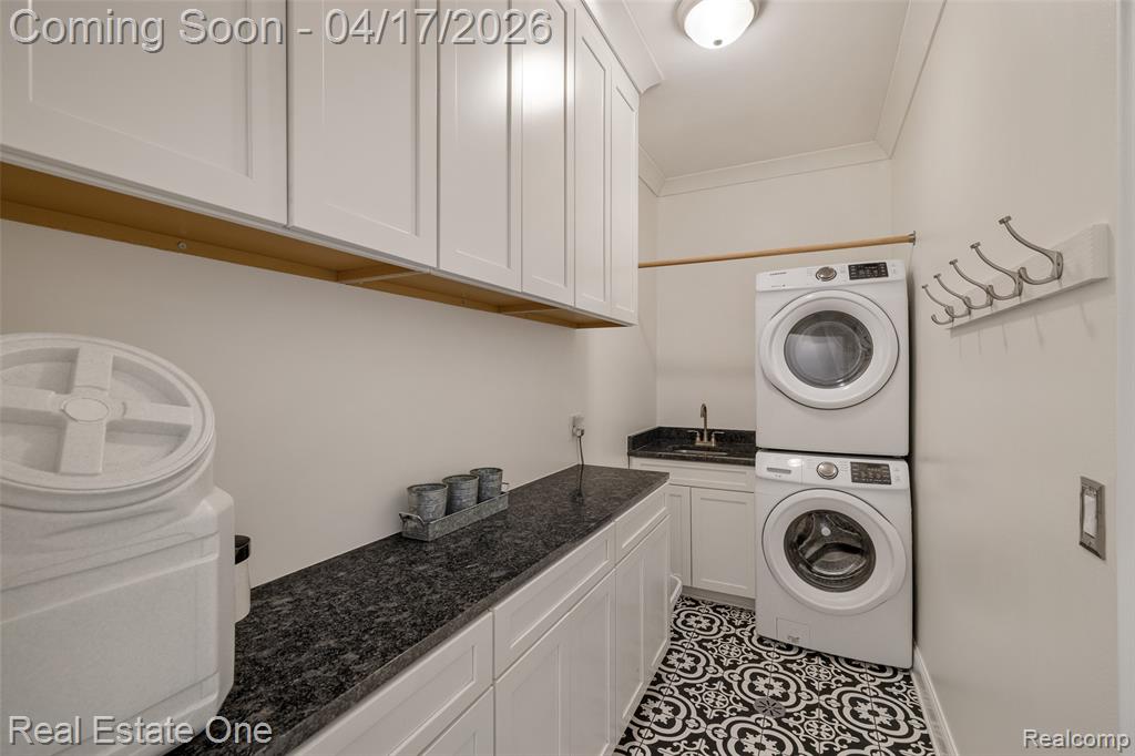 Laundry area with crown molding, cabinet space, stacked washer and clothes dryer, and light tile patterned floors