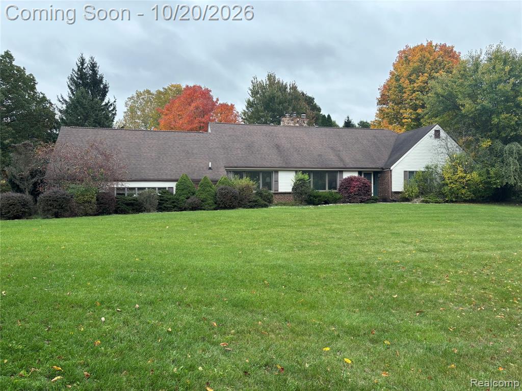 Single-story exterior featuring multi-gabled rooflines, stone chimney, sprawling lawn, and mature landscaping