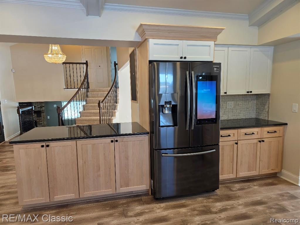 Kitchen featuring stainless steel fridge with ice dispenser, dark wood-style flooring, backsplash, ornamental molding, and a peninsula