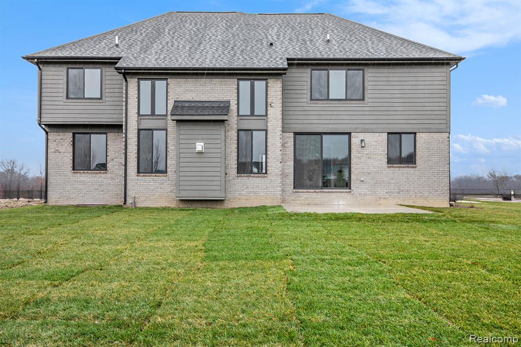 Back of house with a lawn, a shingled roof, brick siding, and a patio area