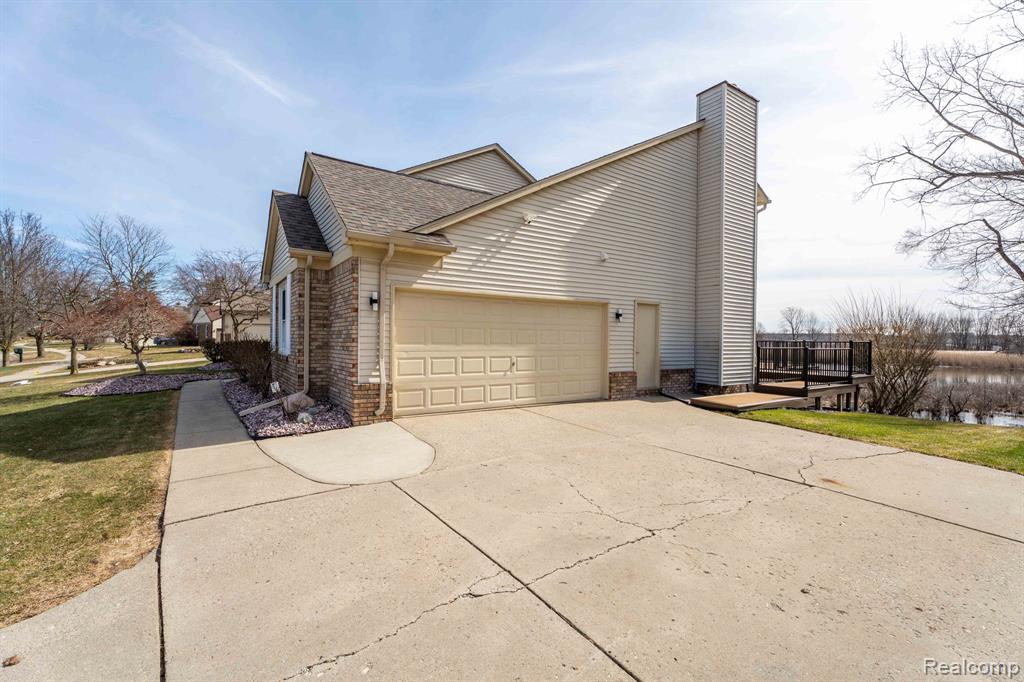 View of home's exterior featuring a deck, driveway, brick siding, an attached garage, and roof with shingles