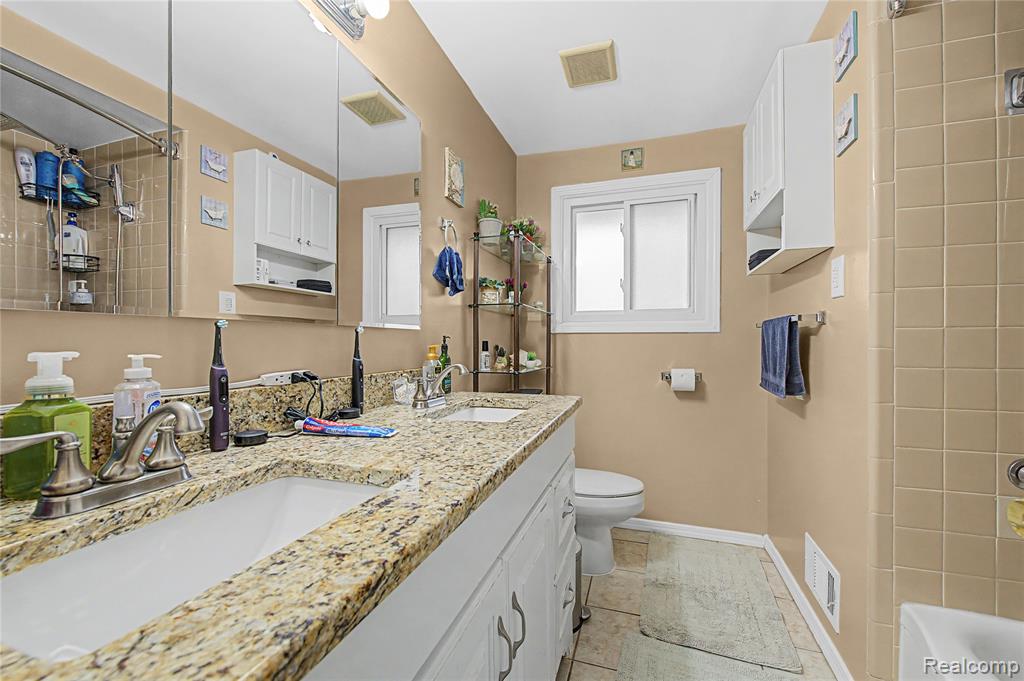 Bathroom featuring double vanity, tiled shower / bath combo, and light tile patterned floors