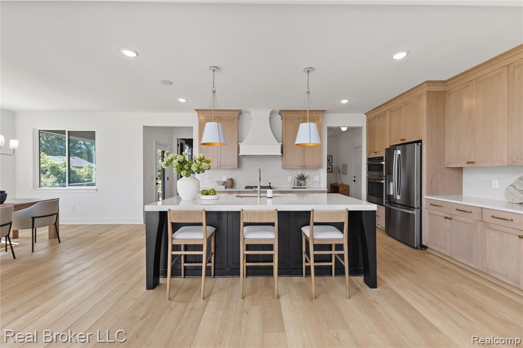 Kitchen featuring light stone countertops, premium range hood, backsplash, light brown cabinetry, and plenty of natural light
