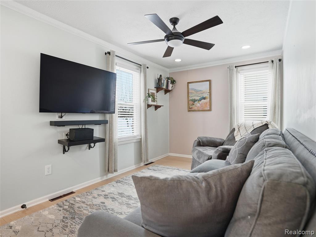 Living room with wood finished floors, a ceiling fan, ornamental molding, and recessed lighting