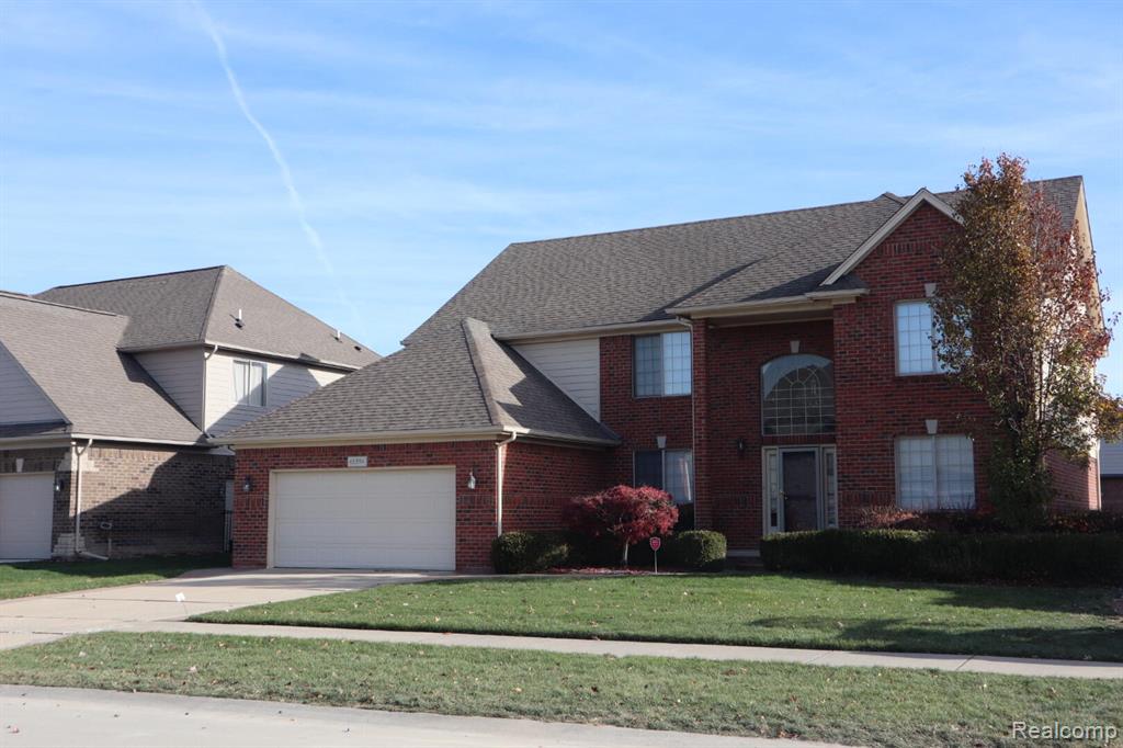 View of front of home with an attached garage, brick siding, a front yard, roof with shingles, and driveway