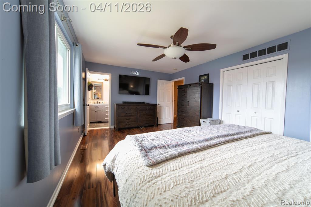 Bedroom with a closet, dark wood-type flooring, ceiling fan, and connected bathroom