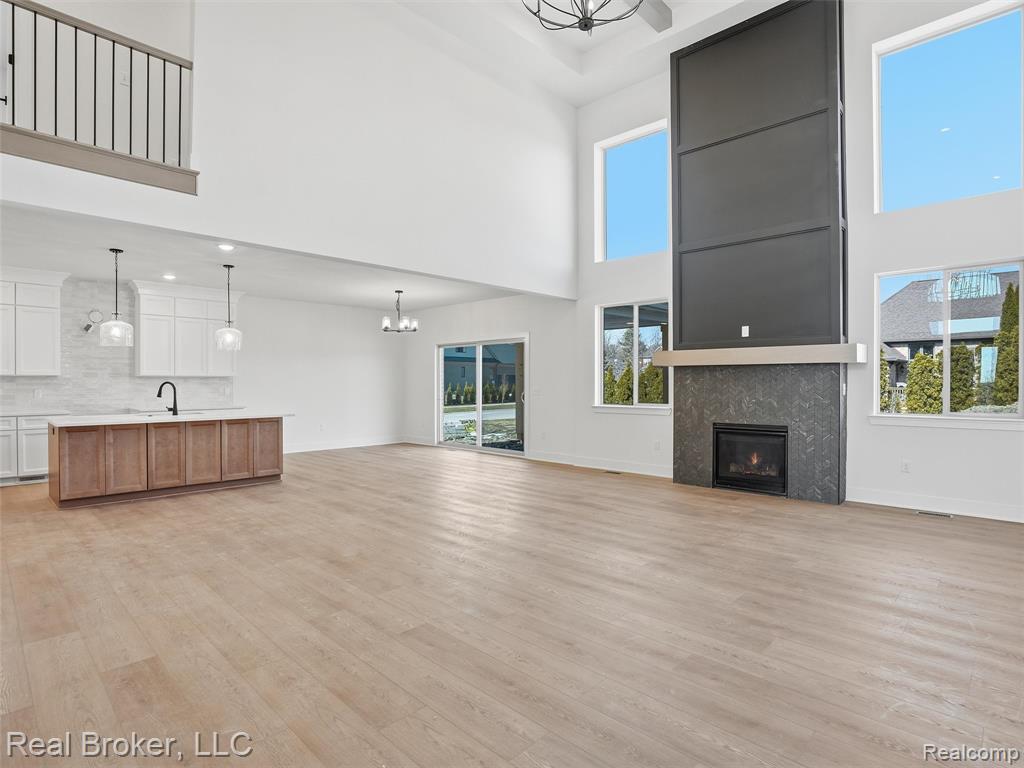 Unfurnished living room featuring a chandelier, a warm lit fireplace, light wood-type flooring, and a high ceiling