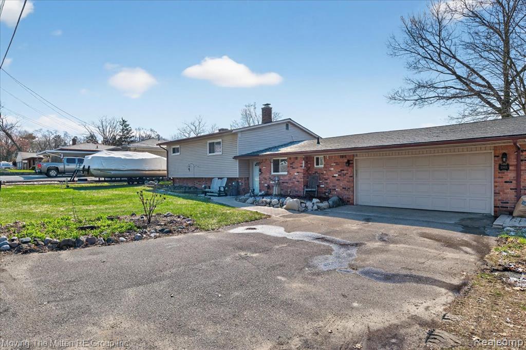 Tri-level home with a chimney, brick siding, a front yard, driveway, and an attached garage