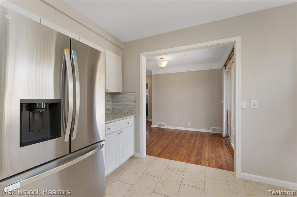 Kitchen featuring stainless steel refrigerator with ice dispenser, white cabinetry, light stone counters, and tasteful backsplash