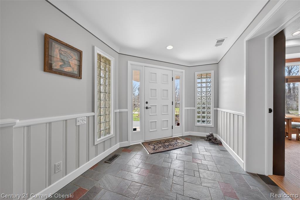 Entrance foyer featuring a wainscoted wall, stone tile floors, a decorative wall, and recessed lighting