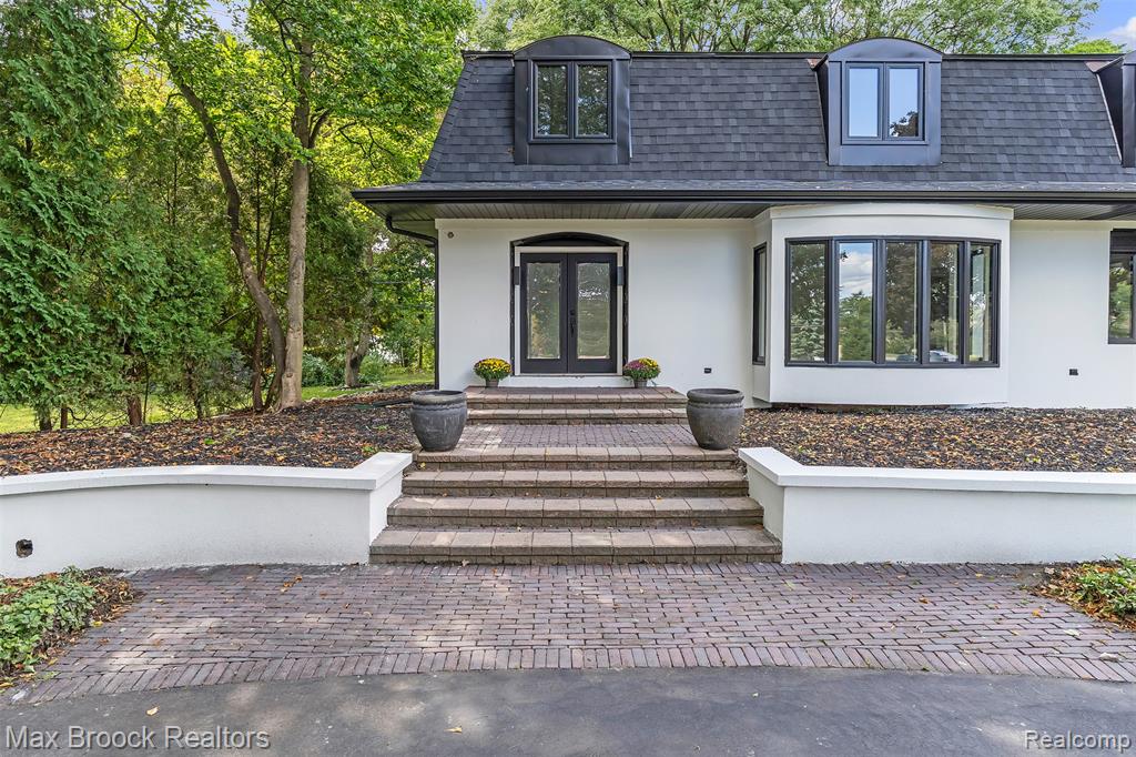 View of exterior entry with roof with shingles, mansard roof, stucco siding, french doors, and a porch