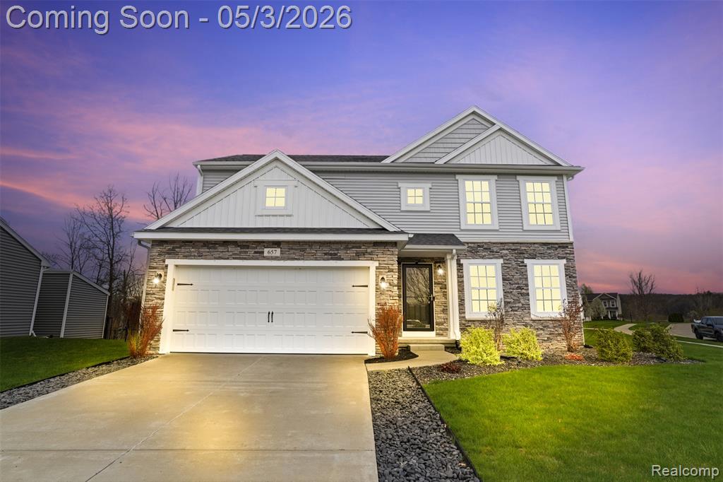 View of front of property featuring stone, siding, concrete driveway, and a front lawn