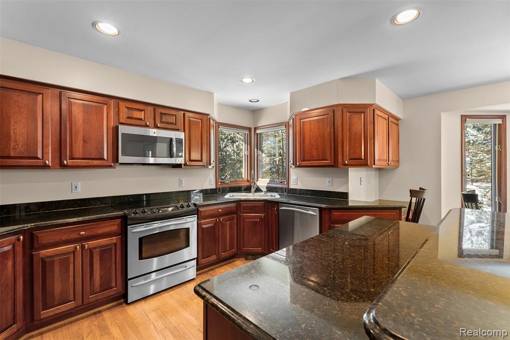 Kitchen featuring stainless steel appliances, dark stone countertops, light wood finished floors, recessed lighting, and brown cabinetry