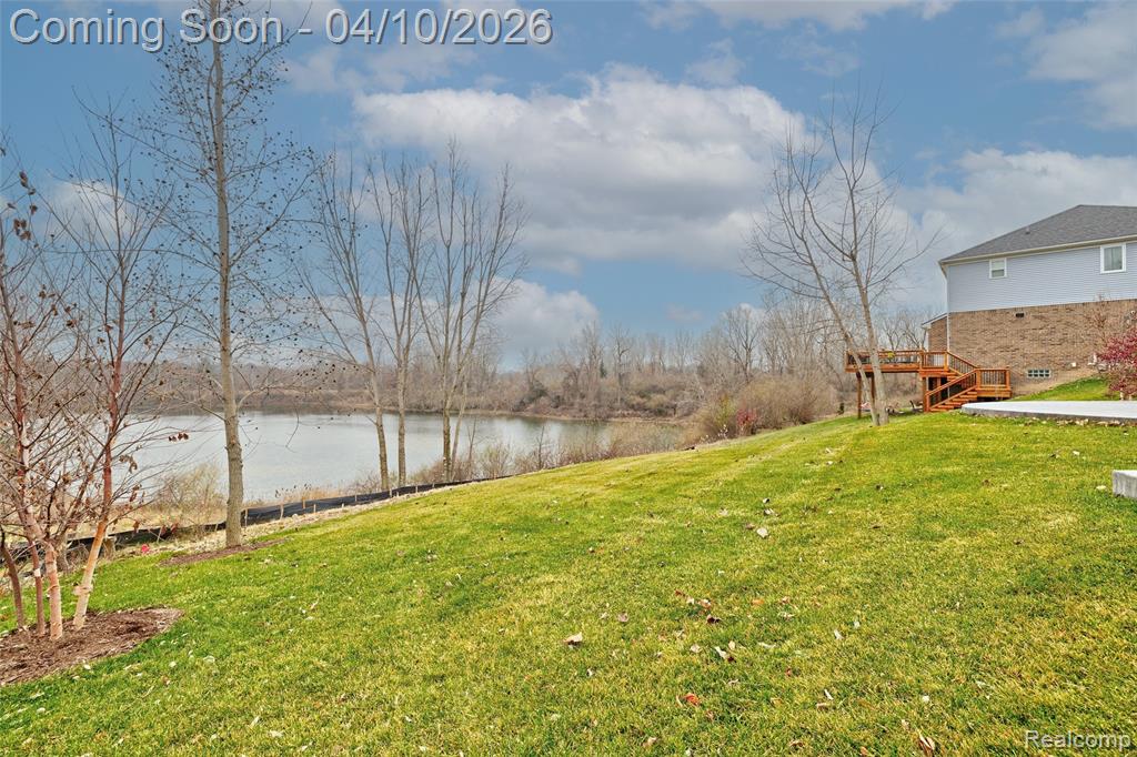 View of green lawn with a deck with water view and stairway