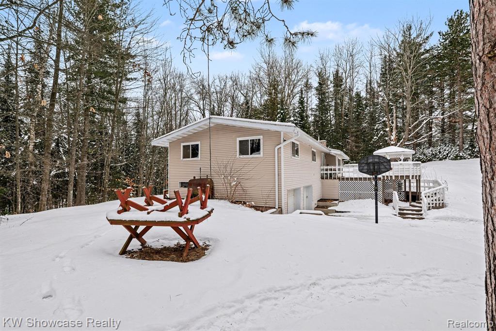 Snow covered property featuring an attached garage, a wooden deck, and view of wooded area